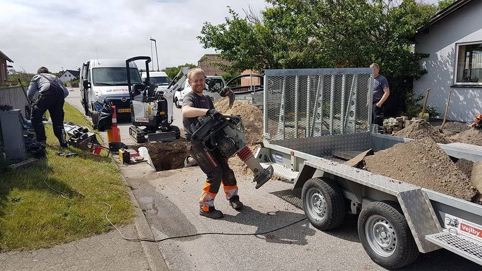 En mand bærer en pose jord på ryggen ved siden af ​​en trailer.