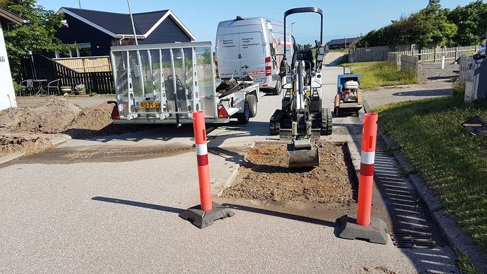 En traktor graver et hul i jorden foran et hus