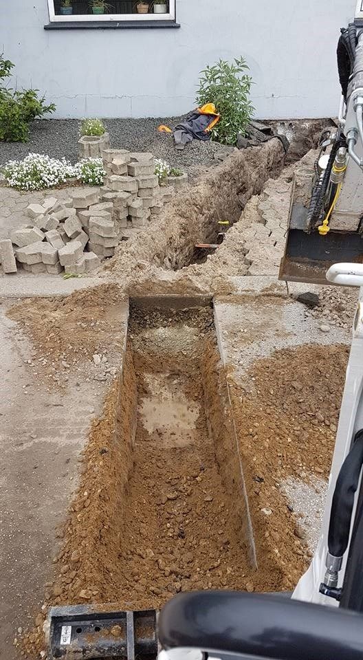 En graver graver et hul i jorden foran et hus.