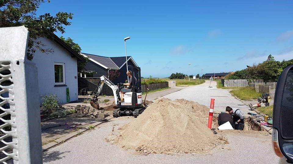 En bulldozer graver et hul i jorden foran et hus