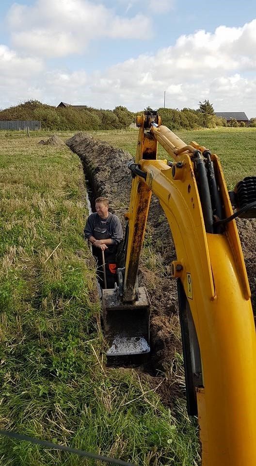 En mand sidder ved siden af ​​en gul gravemaskine på en mark.