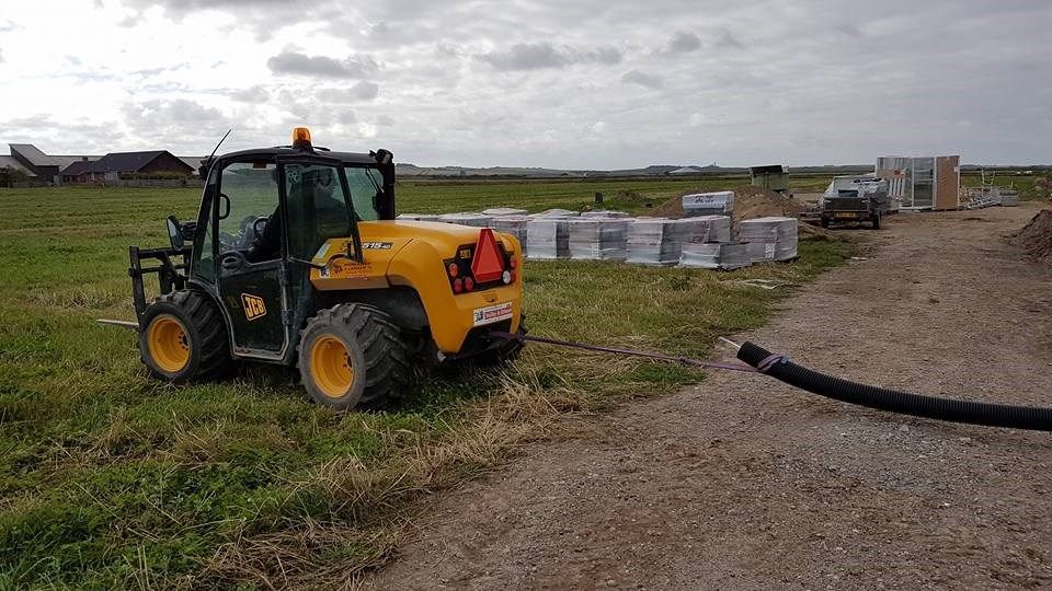 En gul traktor er parkeret på en græsmark ved siden af ​​en slange.