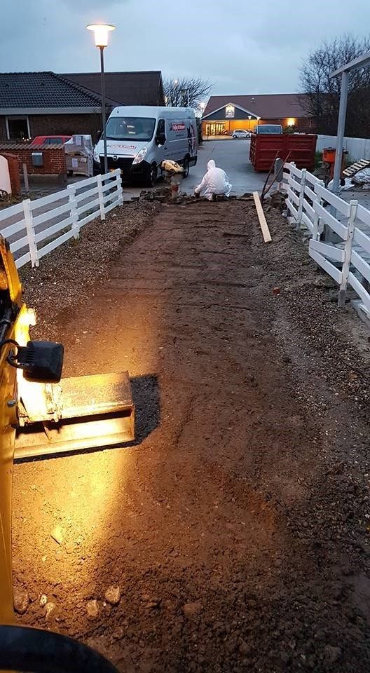 En gul lastbil kører ned ad en grusvej ved siden af ​​et hvidt hegn.