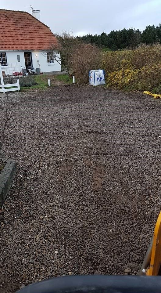 En grusindkørsel med et hvidt hus i baggrunden.