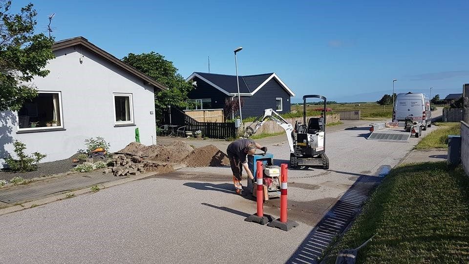 En mand er ved at grave et hul i jorden foran et hus.