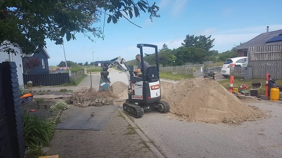 En mand kører en lille gravemaskine på en grusvej.