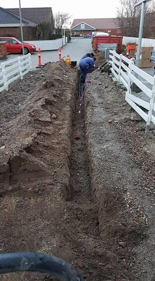 En mand graver et hul i jorden ved siden af ​​et hvidt hegn.