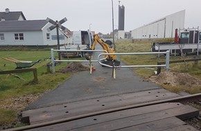 En gul gravemaskine arbejder på en jernbaneoverskæring.