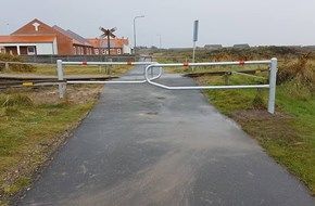 En vej med et hegn på siden af det og en jernbaneoverskæring i baggrunden.