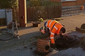 En mand i en orange sikkerhedsvest graver et hul i jorden.