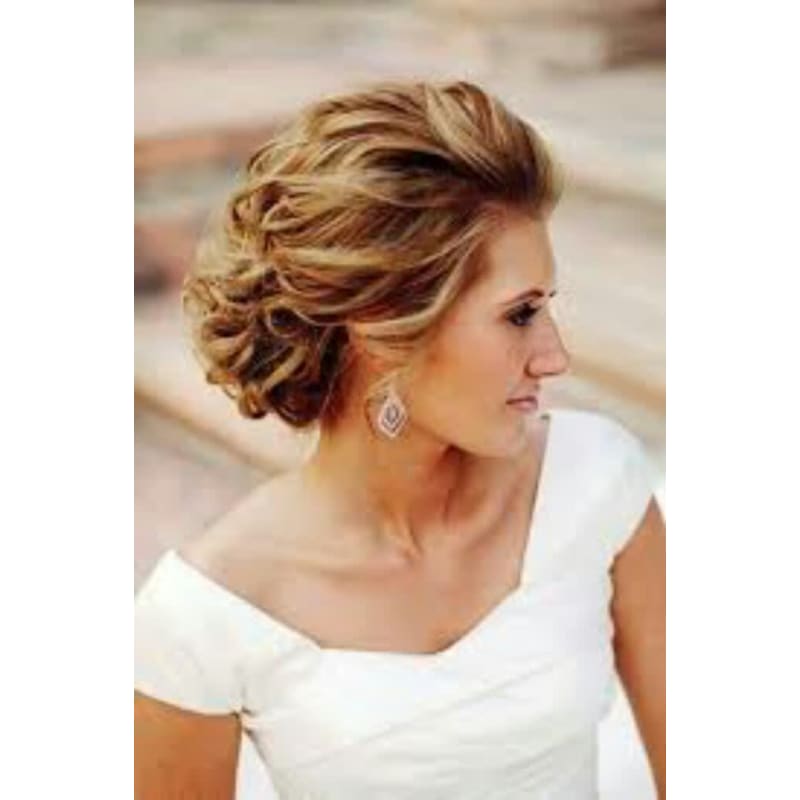 A woman in a white dress is wearing a bun and earrings.