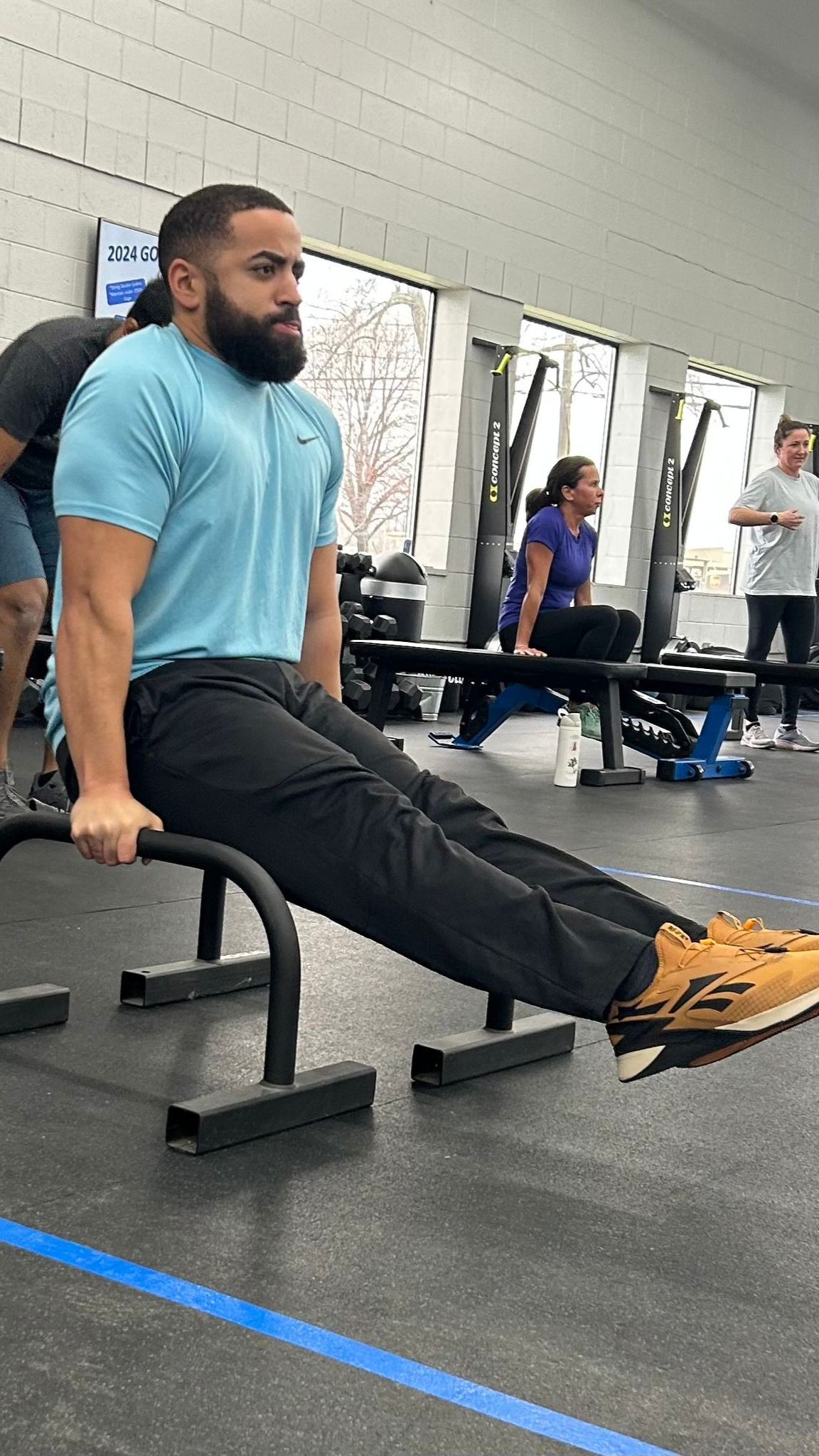 Man doing a dip exercise on parallel bars in a gym. He is wearing a blue shirt and black pants.