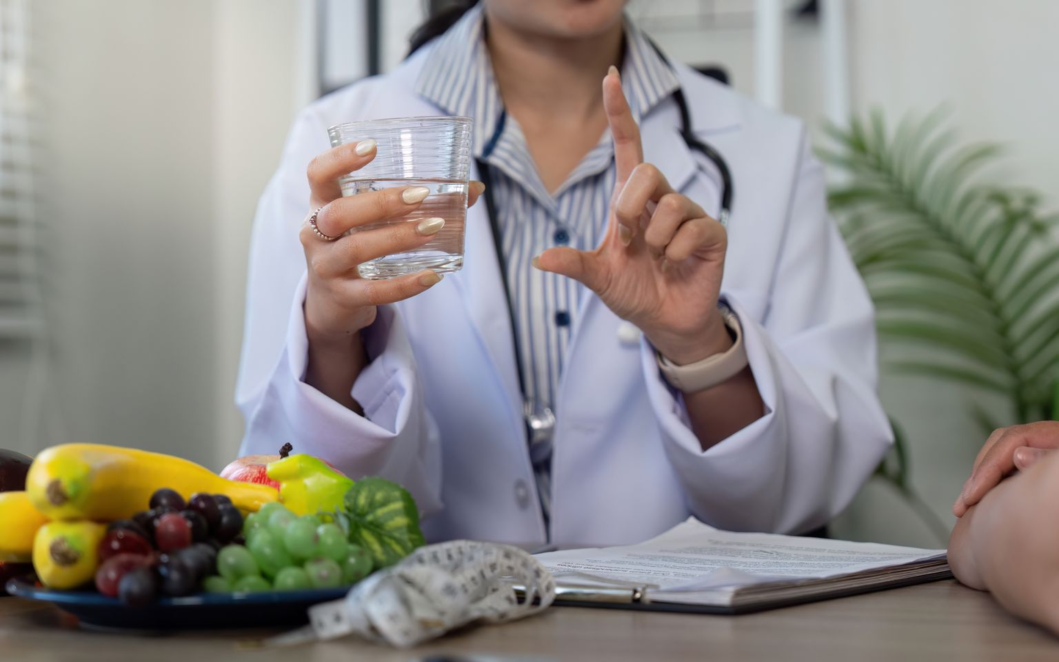 Doctor with water glass and fruit plate gesturing, consulting with a patient at a desk.