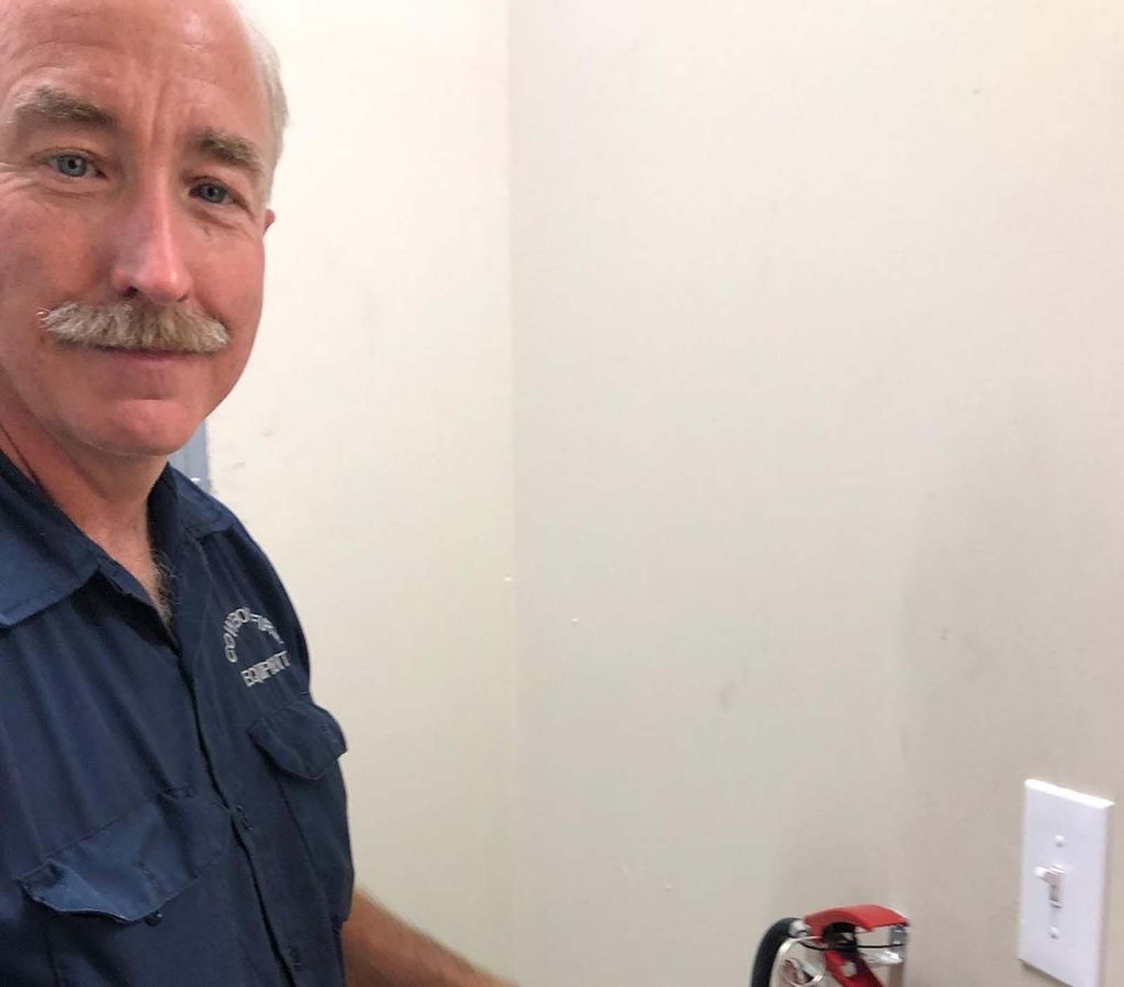 A man with a mustache is holding a fire extinguisher in a room.