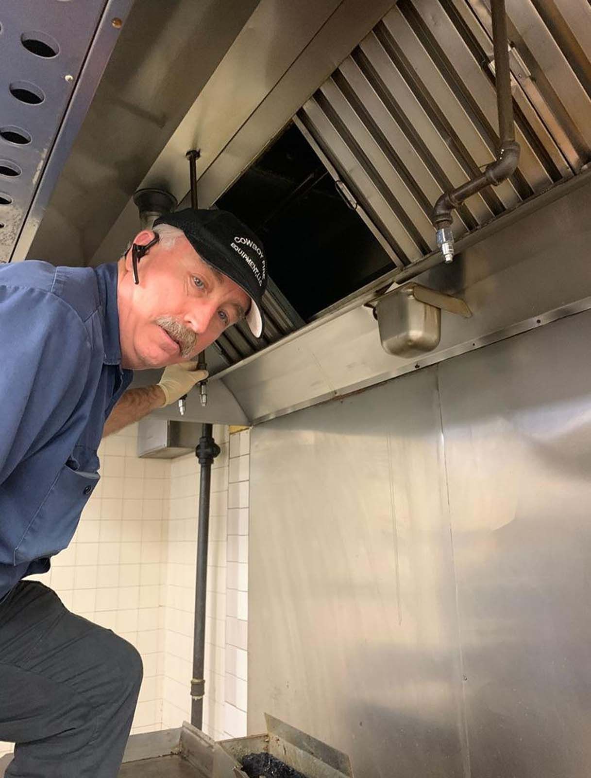 A man in a blue shirt and black hat is working in a kitchen.