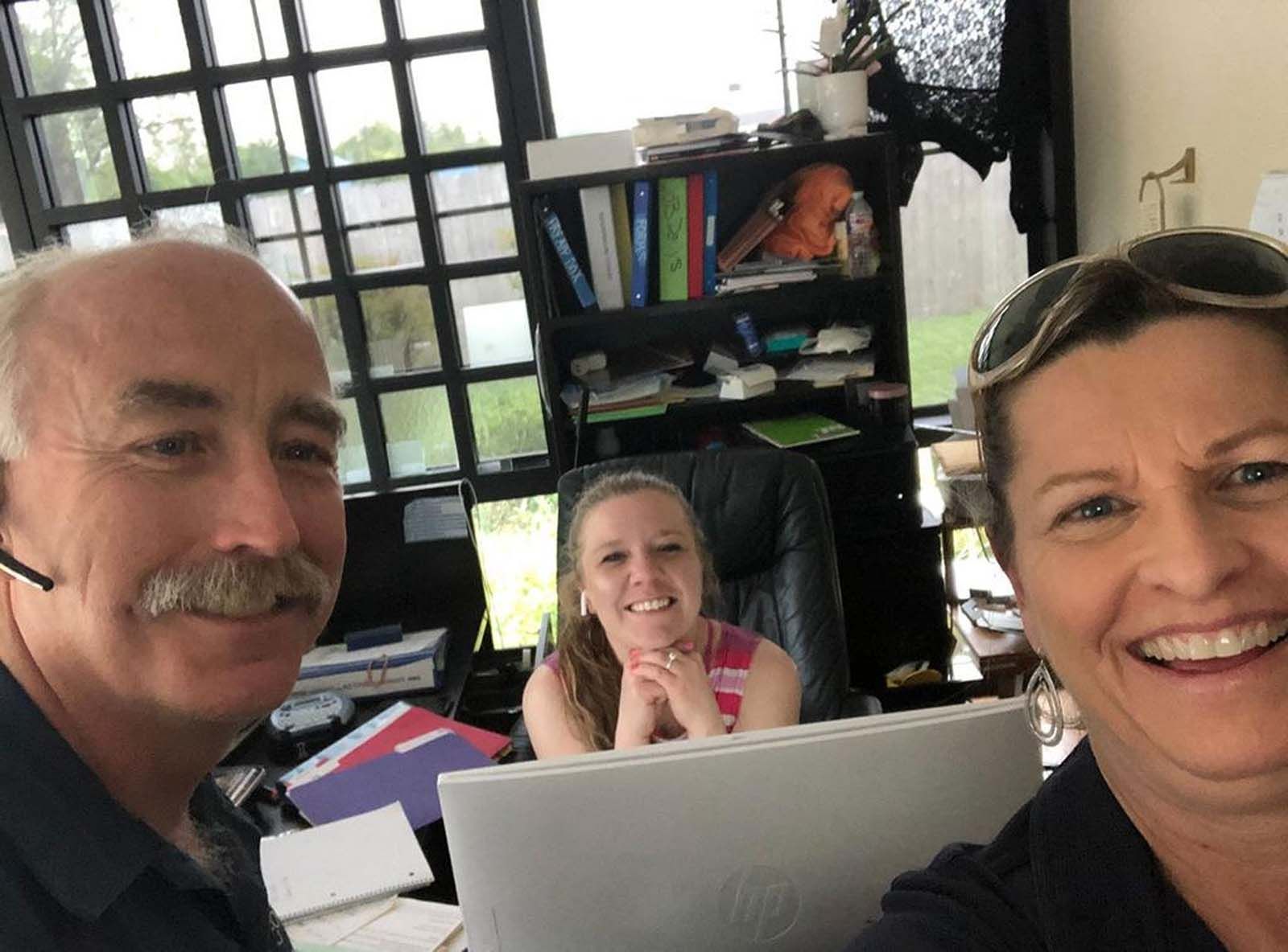A man and two women are smiling in front of a laptop
