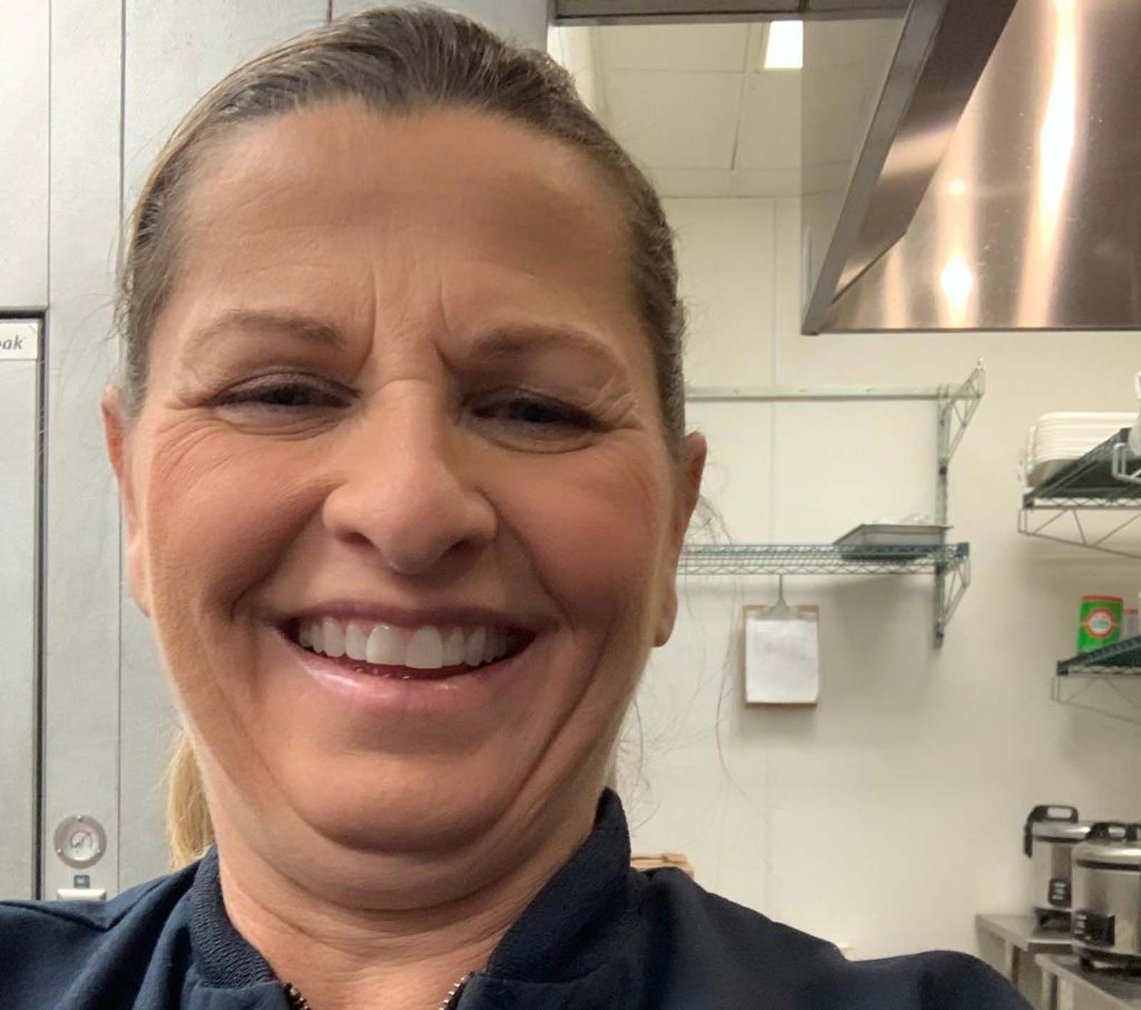A woman is smiling in a kitchen with a stainless steel hood