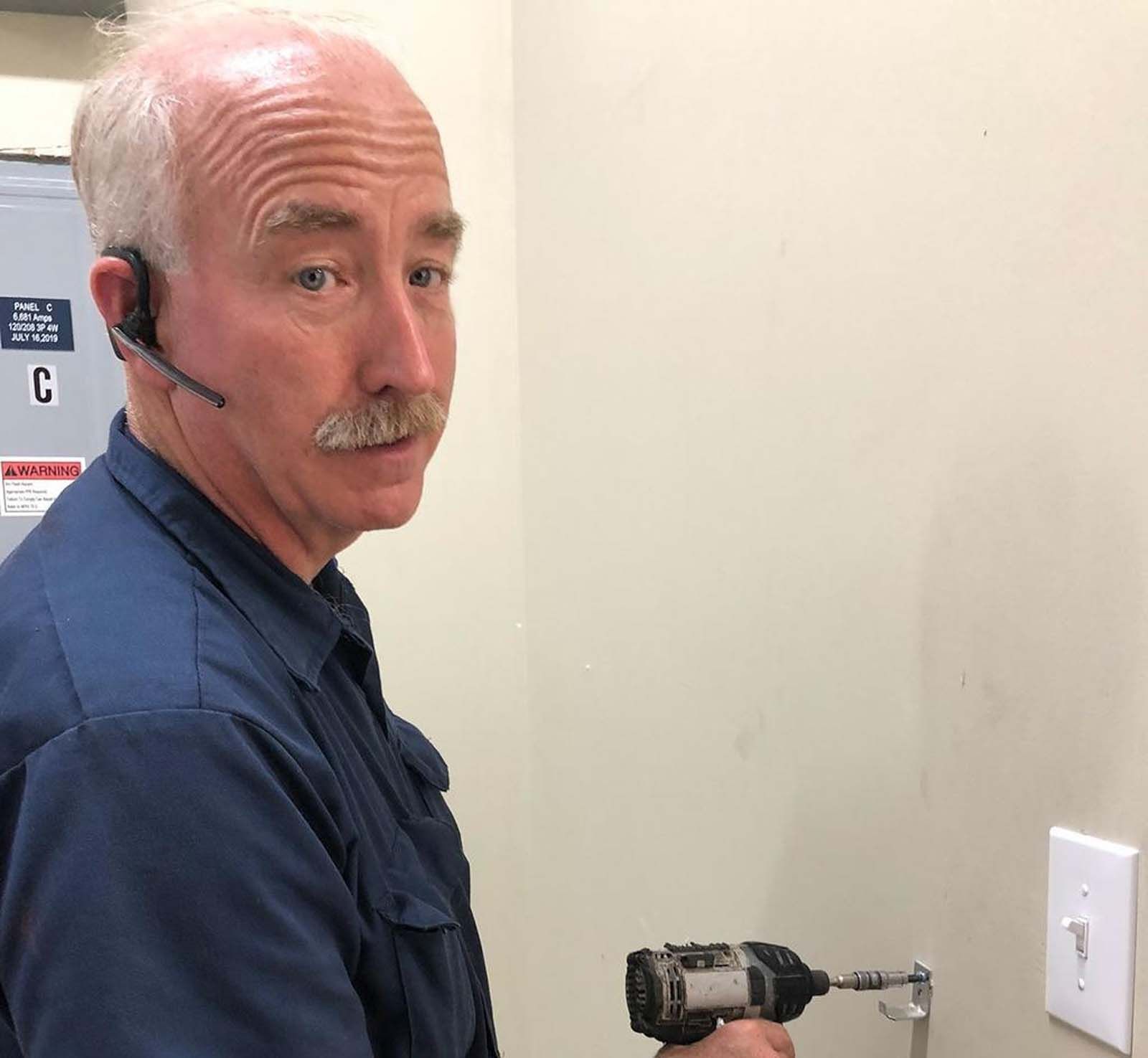 A man wearing a headset is using a drill to fix a light switch