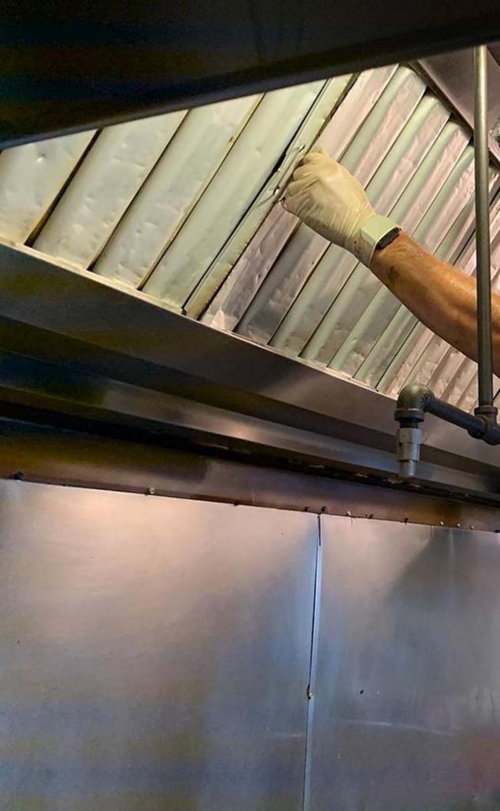 A person wearing gloves is working on a hood in a kitchen.