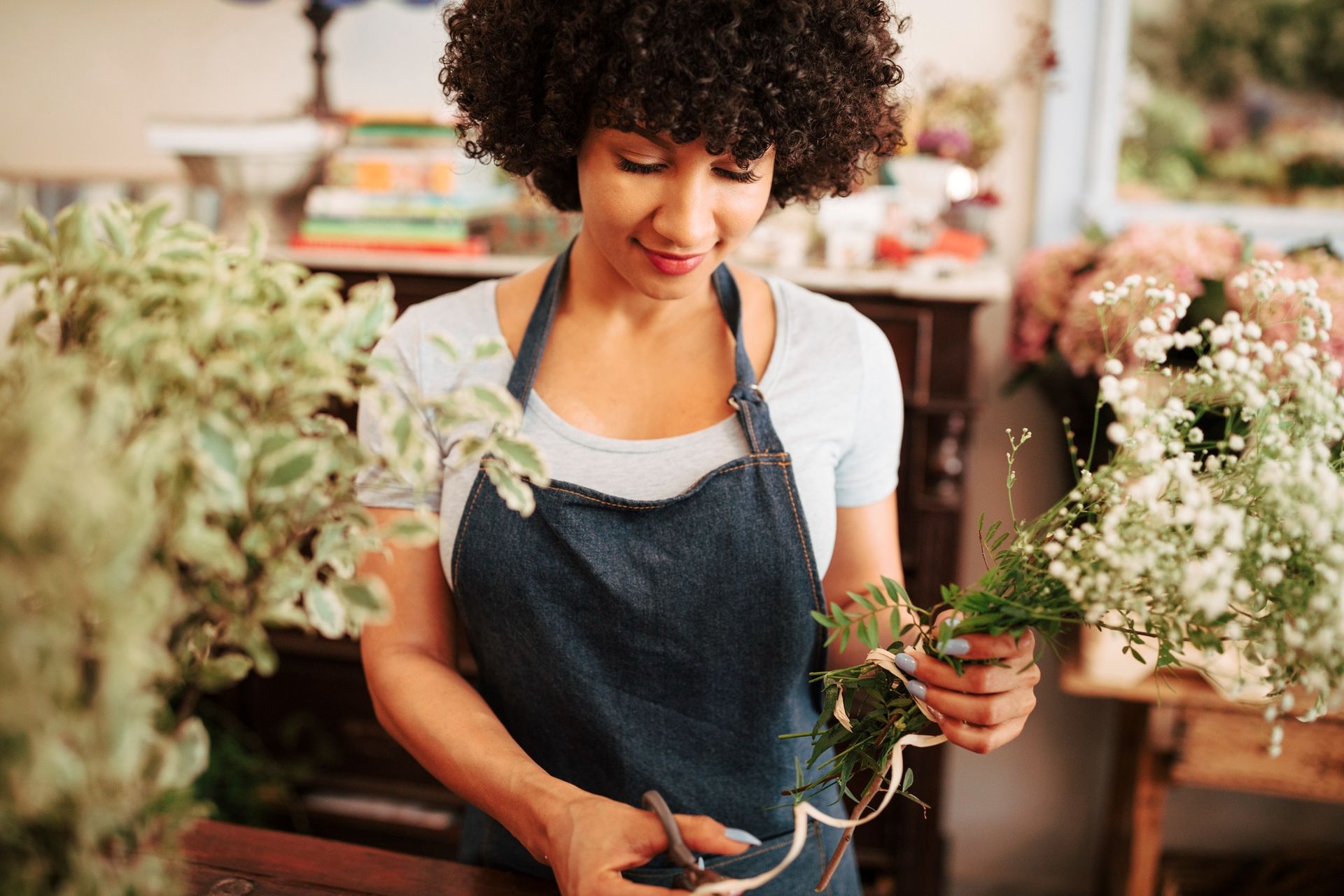 A woman in an apron is cutting flowers in a flower shop.
