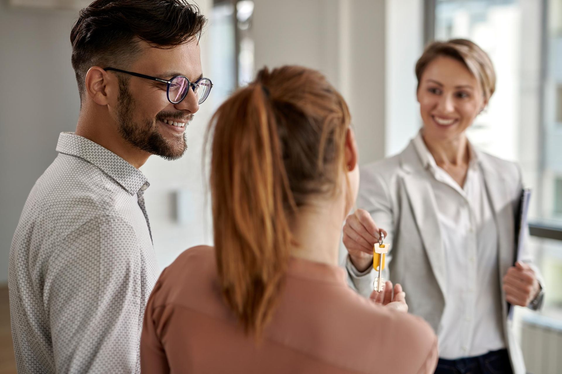 A man and a woman are standing next to each other in a room . the woman is holding the keys to the house.