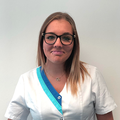 Une personne portant des lunettes à monture noire et un uniforme blanc avec des bordures turquoise et bleues.