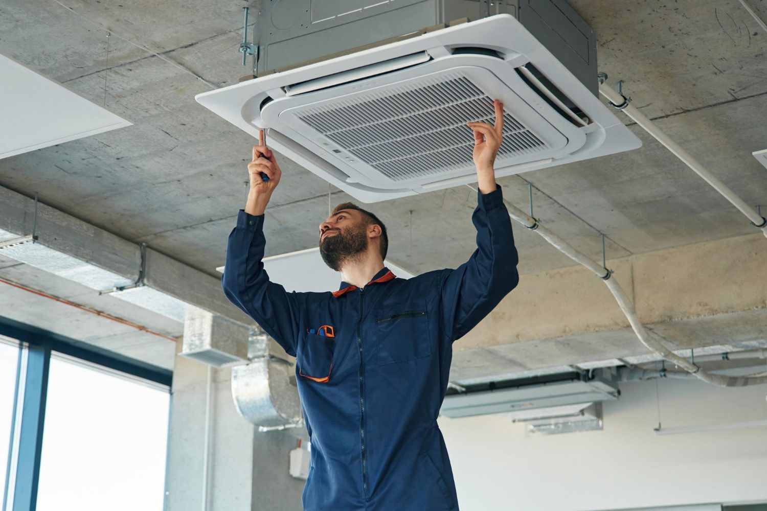 Technician installing a ceiling cassette air conditioner in a modern industrial space