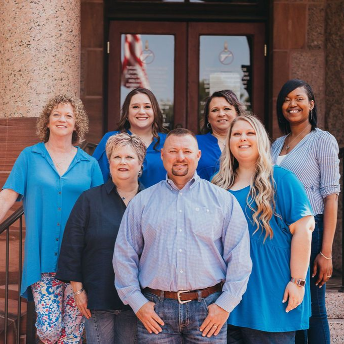 Group of seven people standing together outside a building entrance, smiling at the camera.
