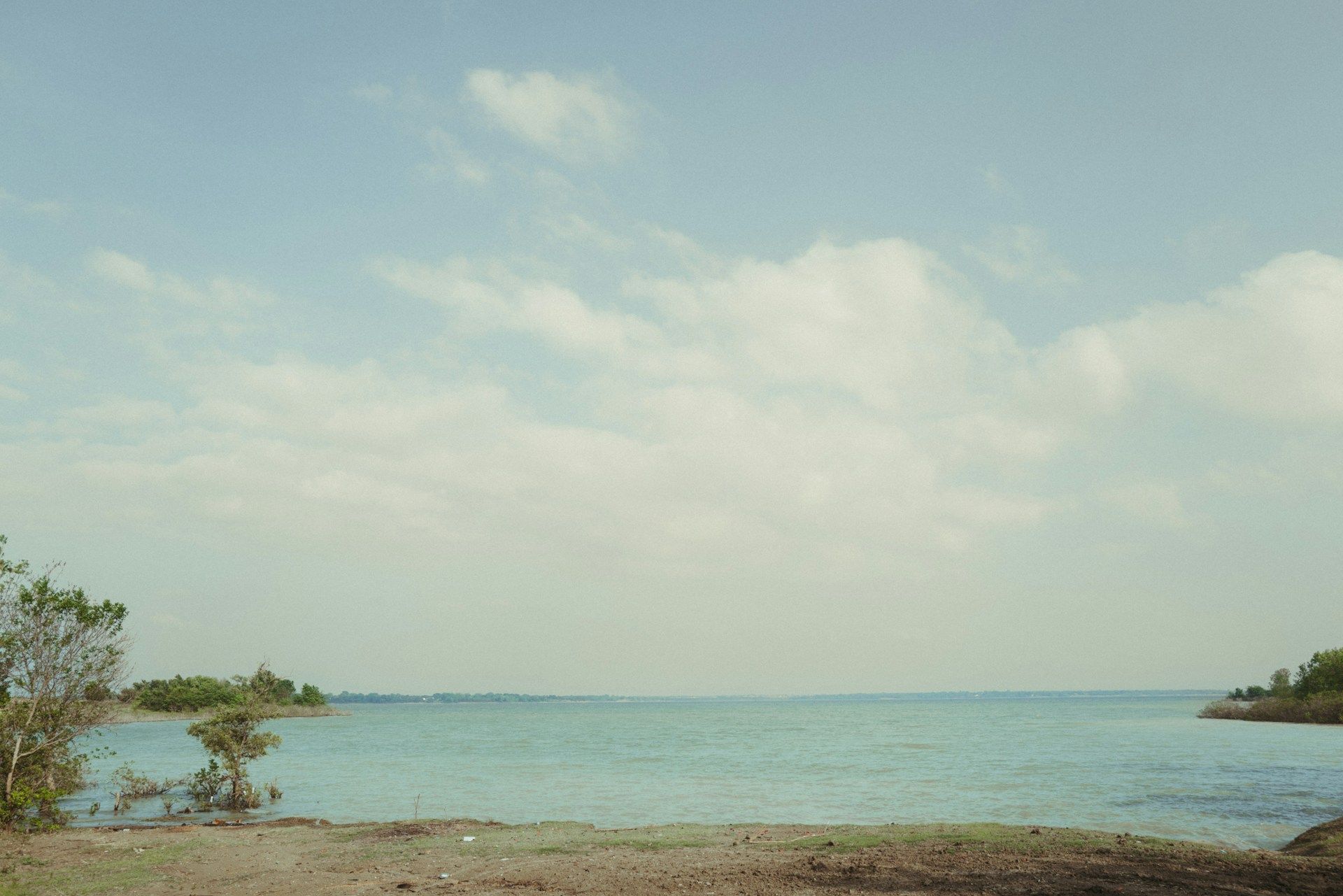 Calm turquoise sea under a pale blue sky with scattered clouds and a rocky shoreline