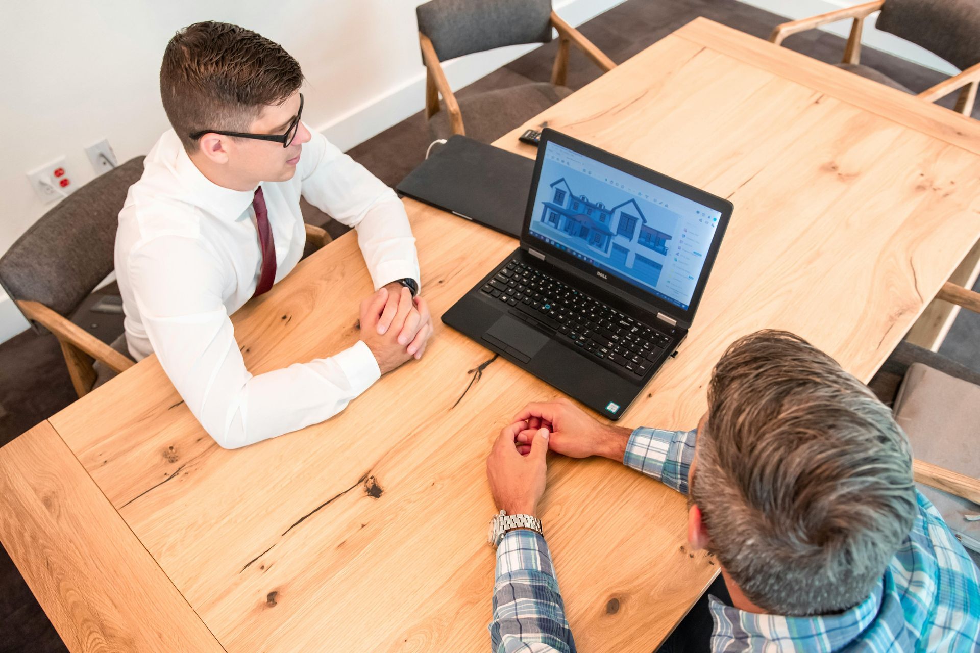Two people in a meeting looking at a laptop on a wooden table