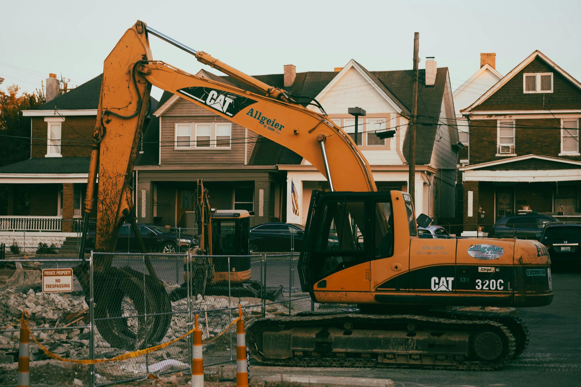 Yellow CAT excavator working in front of a row of houses with a gravel pile in the foreground
