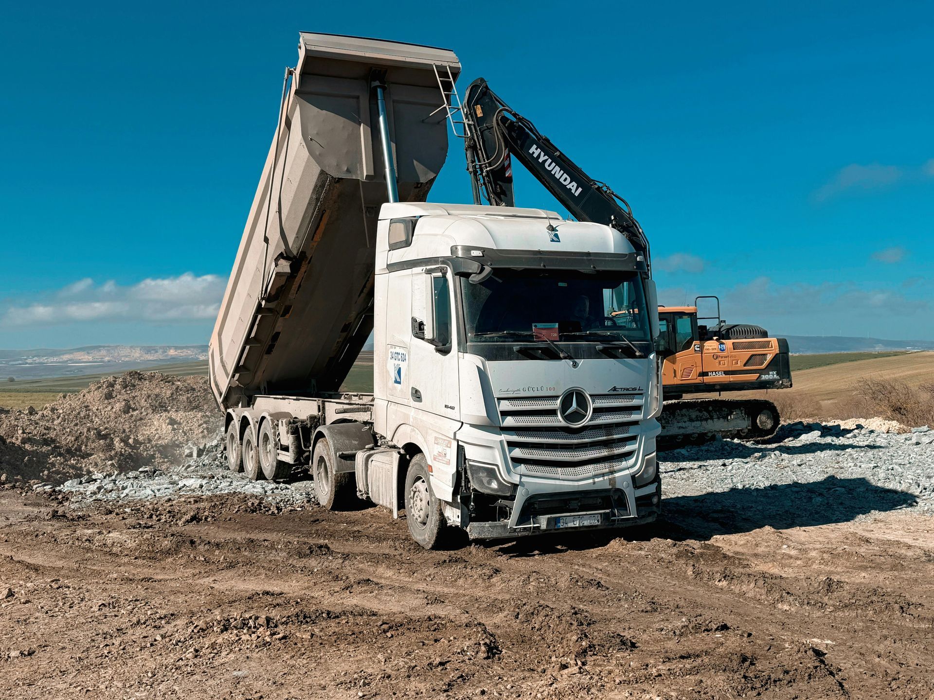 White dump truck tipping gravel at a construction site with an excavator in the background