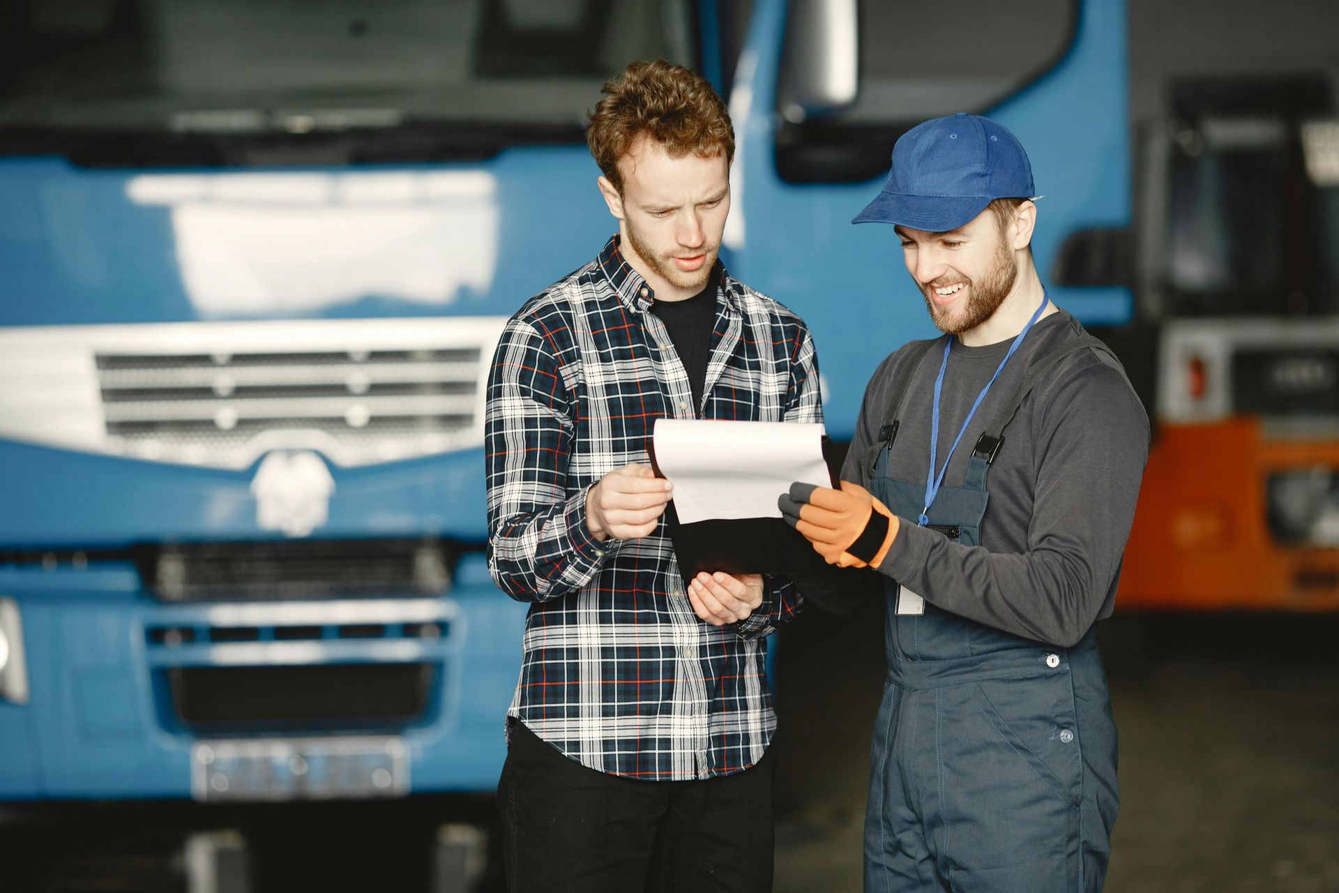 Two mechanics reviewing a clipboard in front of a blue truck in a garage