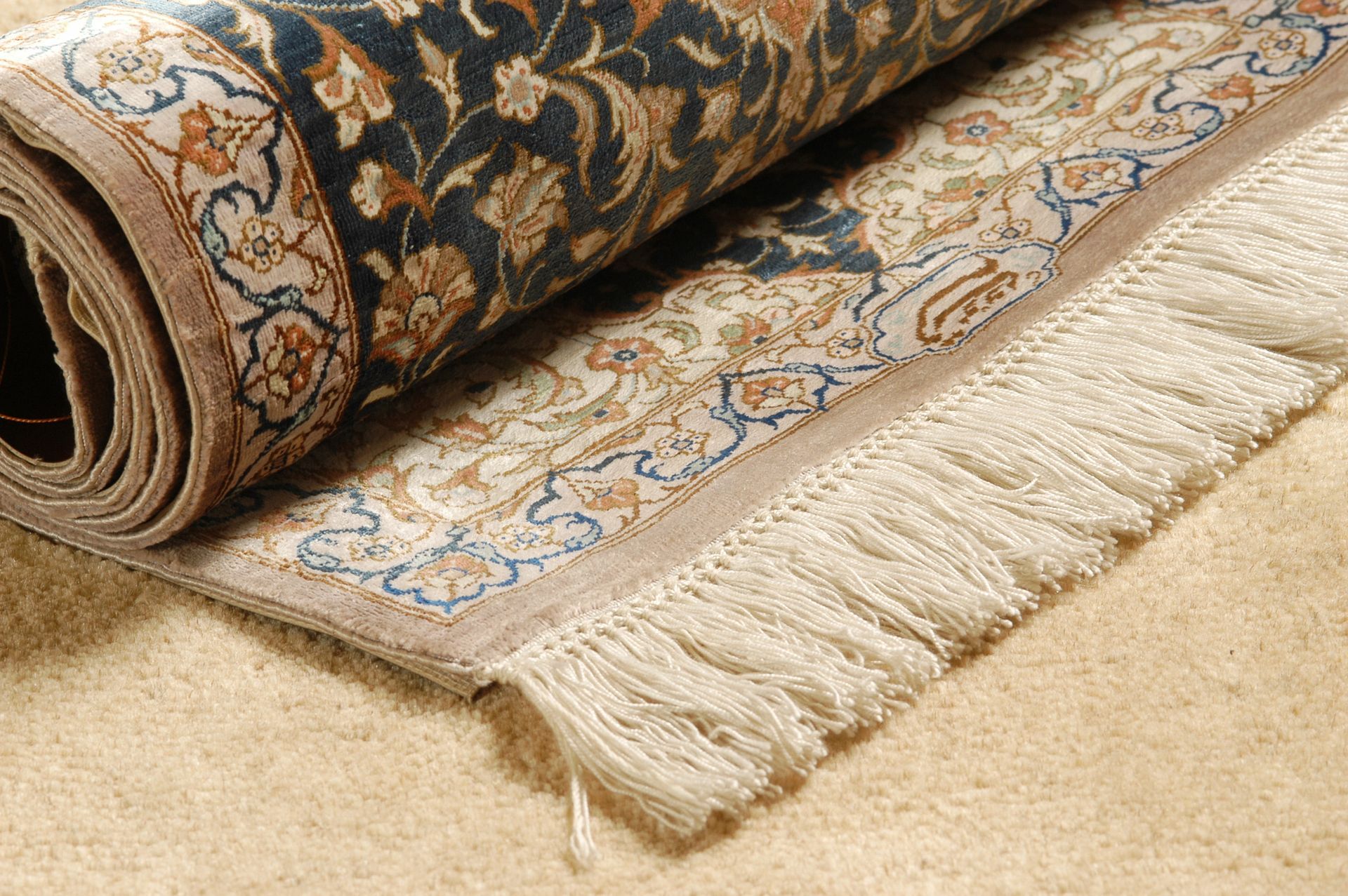 Alfombra enrollada con estampado beige y azul marino y flecos sobre una alfombra clara.