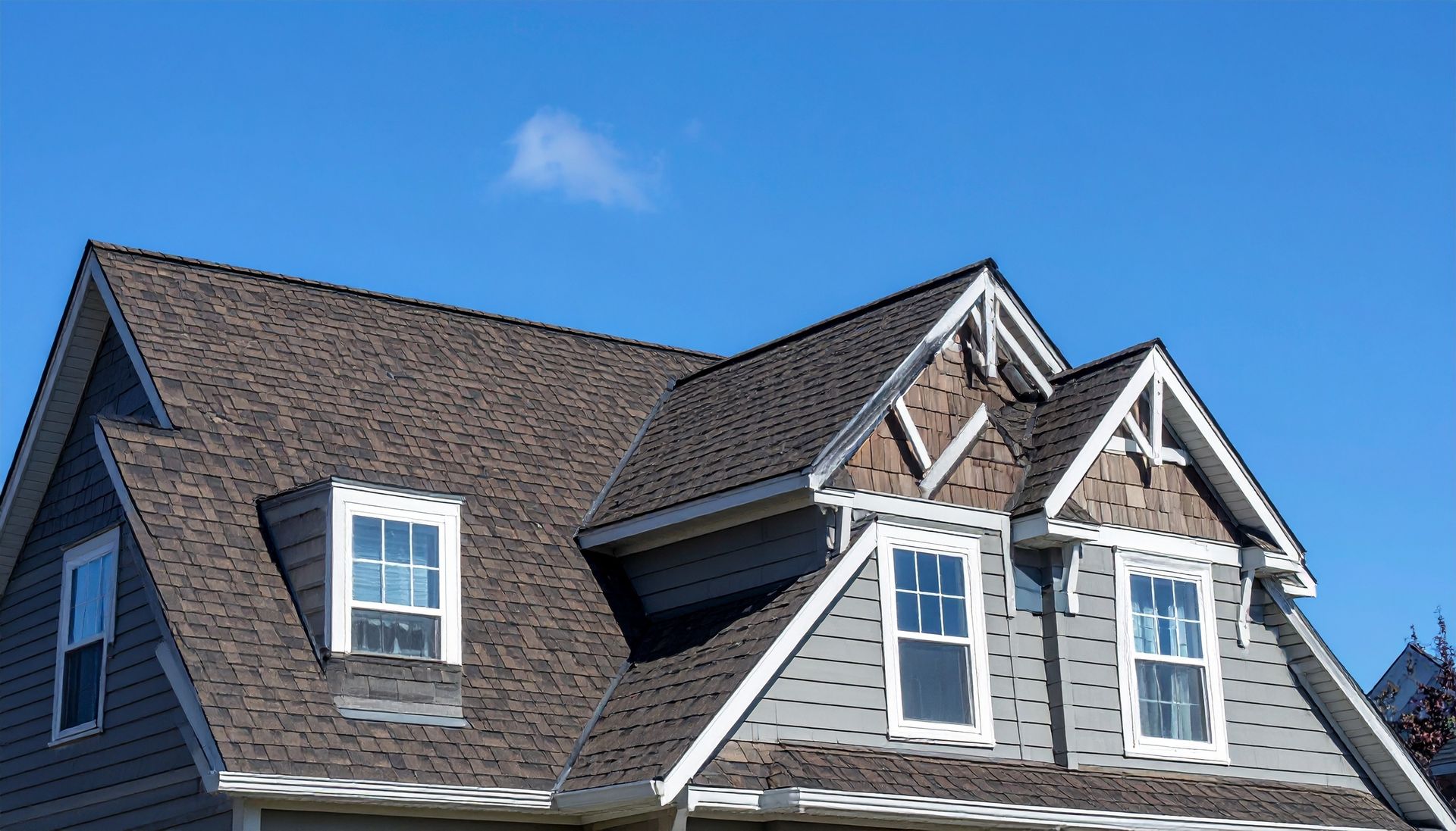 The upper levels and peaked, shingled roof of a dark-gray house against a bright blue sky.