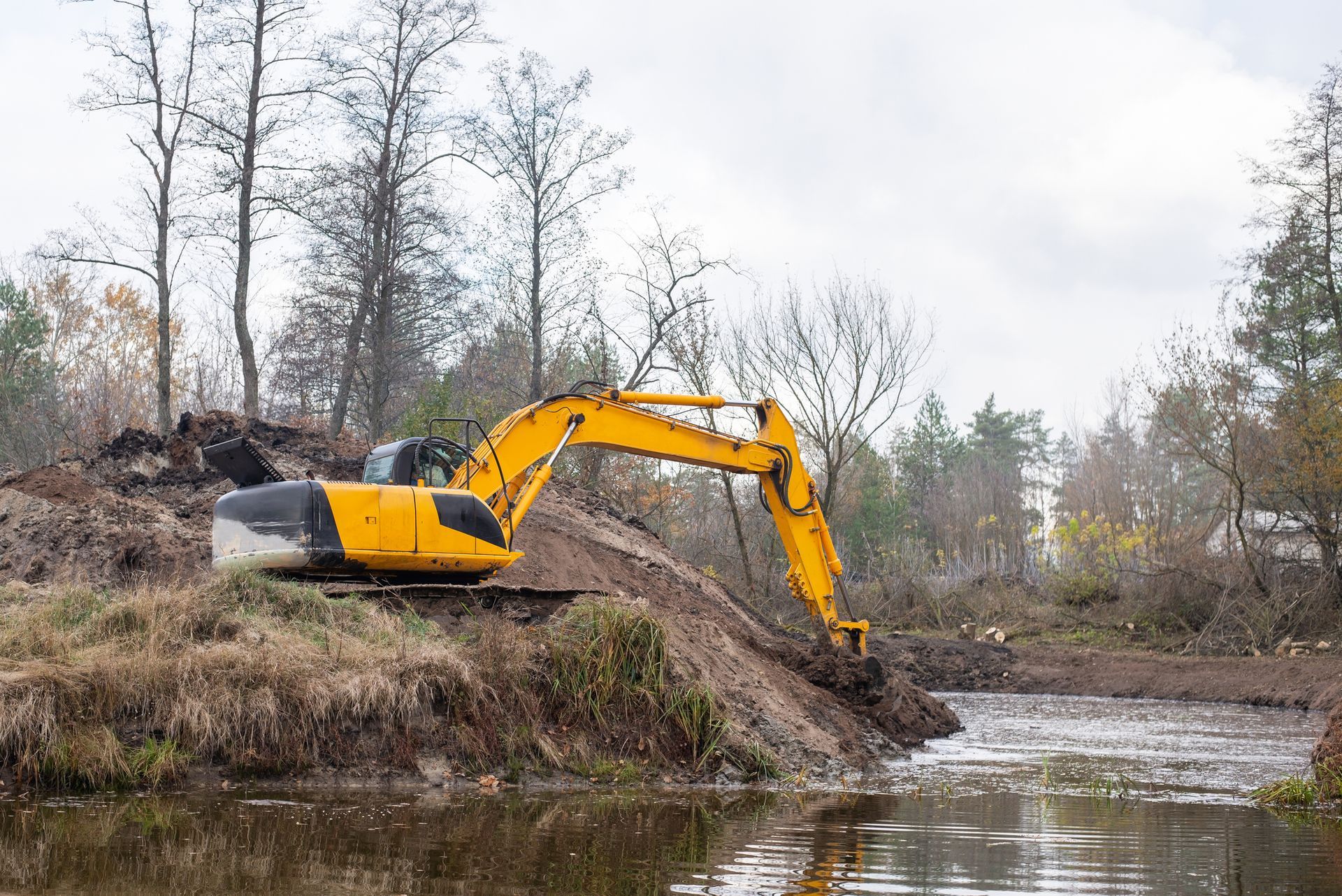 A yellow excavator is digging a hole in the middle of a river.