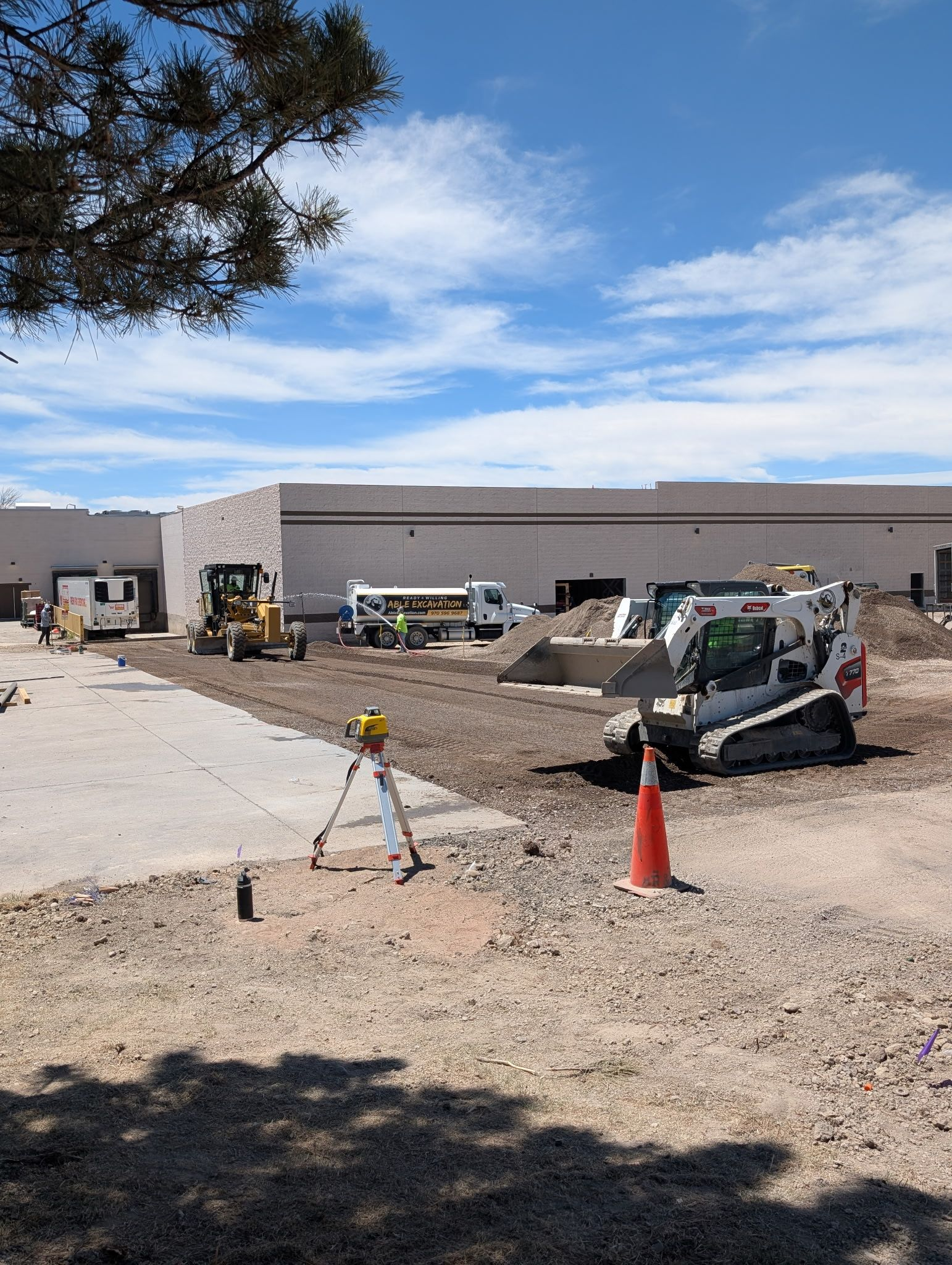 Construction site with parked equipment, cones, and a partially built commercial building under a blue sky