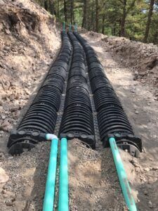 Three rows of black, ridged underground drainage chambers installed in a trench, connected by green PVC piping.