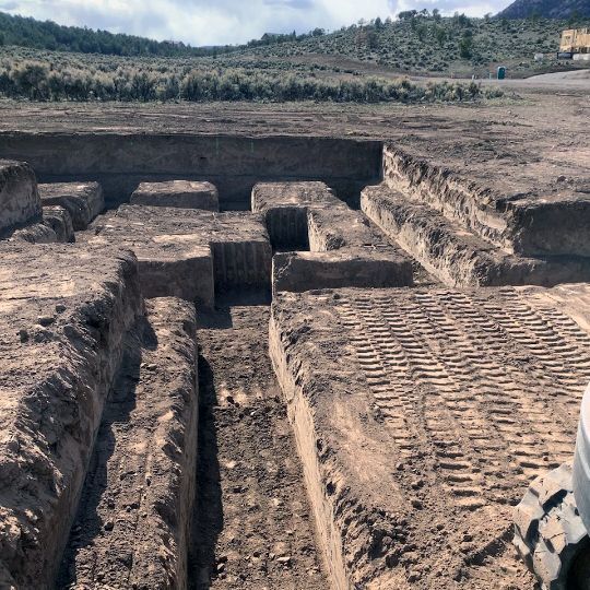 Excavated earthen trenches and rectangular pits at an archaeological dig site in a barren landscape