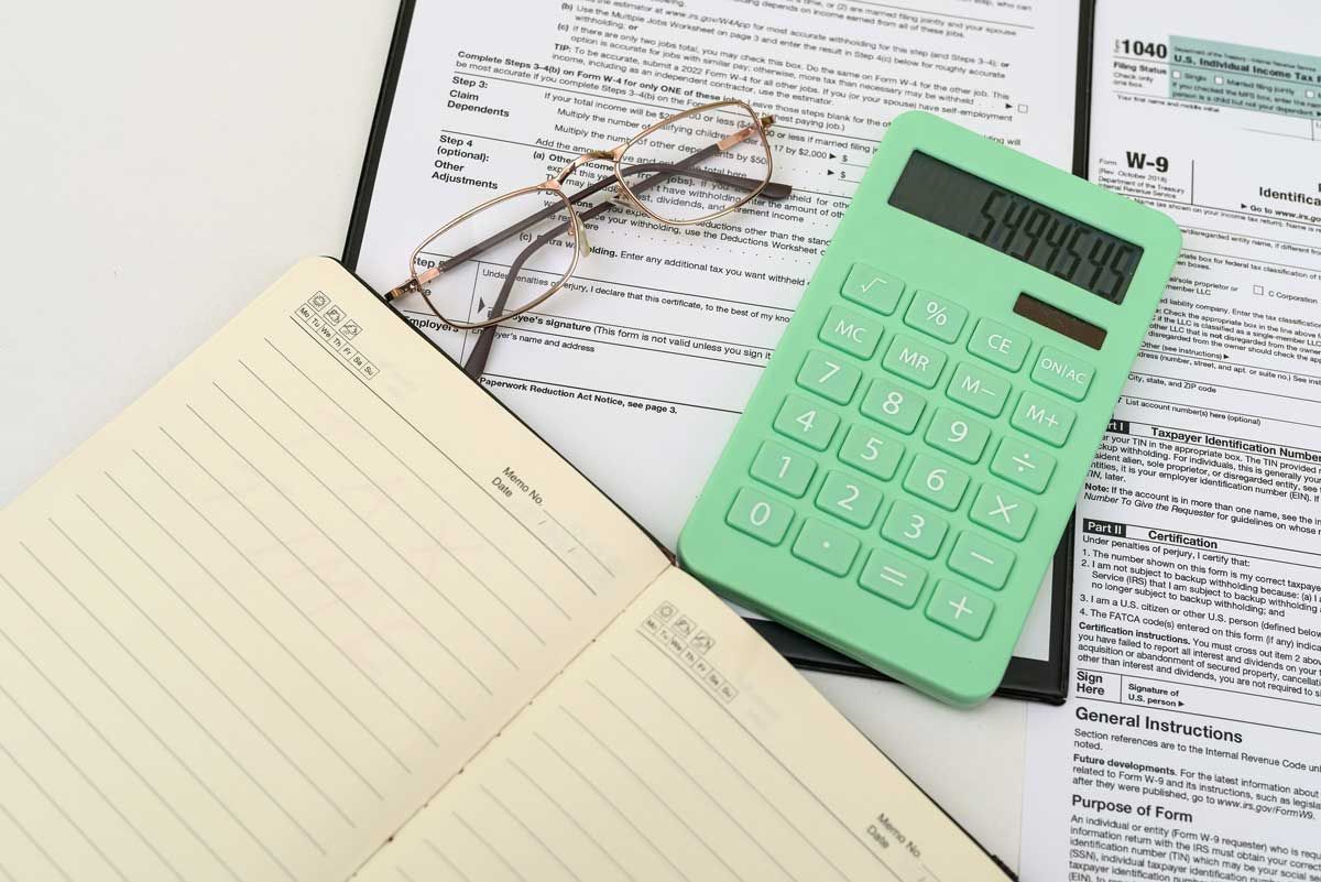 Green calculator, glasses, notebook, and documents on a white surface, suggesting financial tasks.