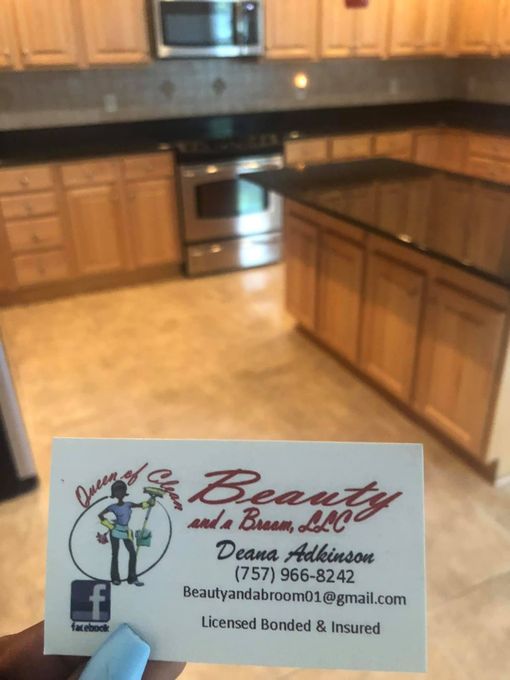 A business card for Beauty and a Broom, LLC, held in front of a clean, modern kitchen with light wood cabinets.