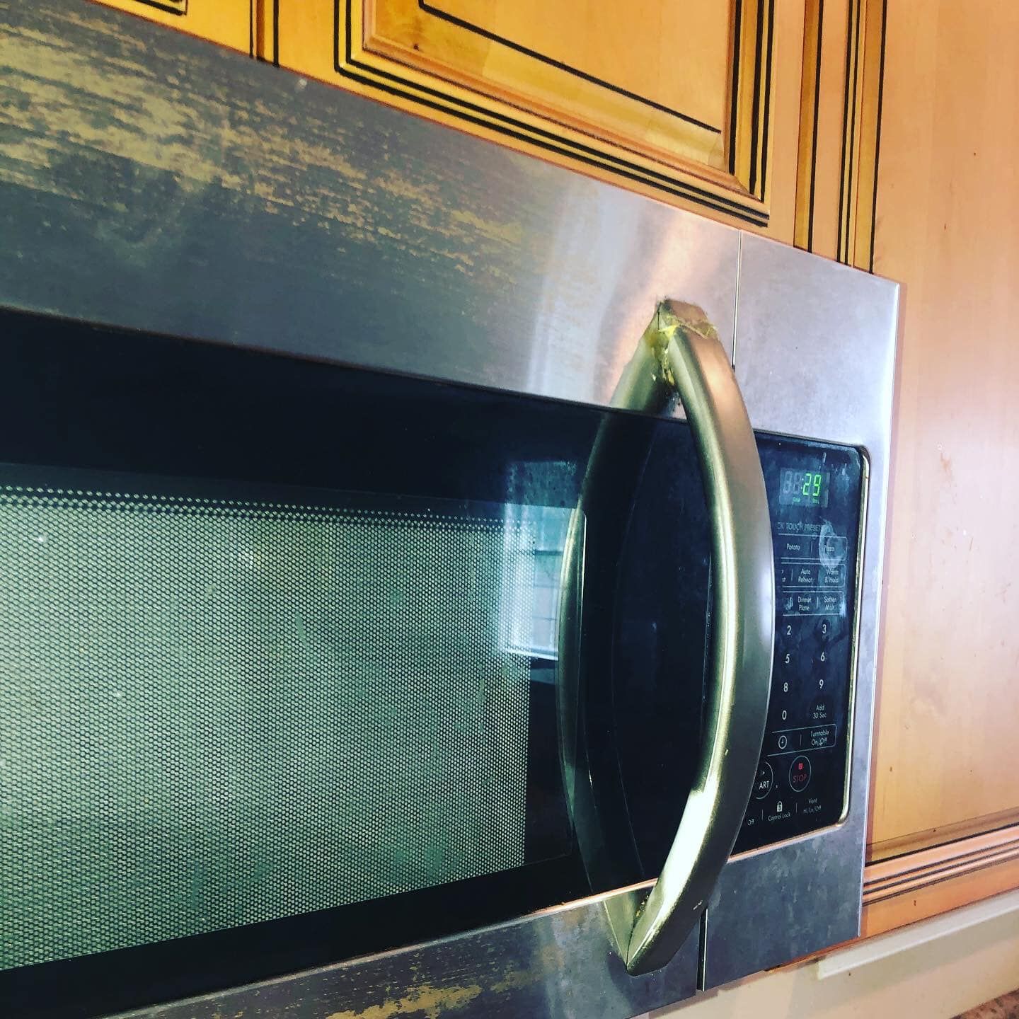 A stainless steel over-the-range microwave with a handle, mounted beneath wooden kitchen cabinets.