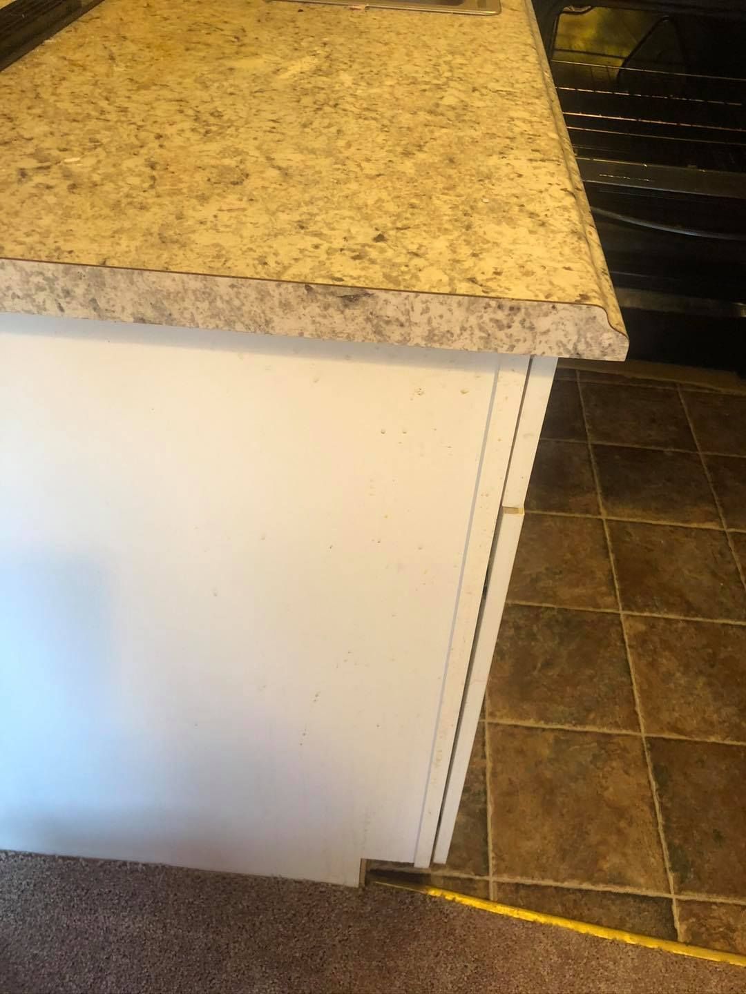 A kitchen counter with speckled laminate top and white side panel, bordering the edge of a carpeted floor.