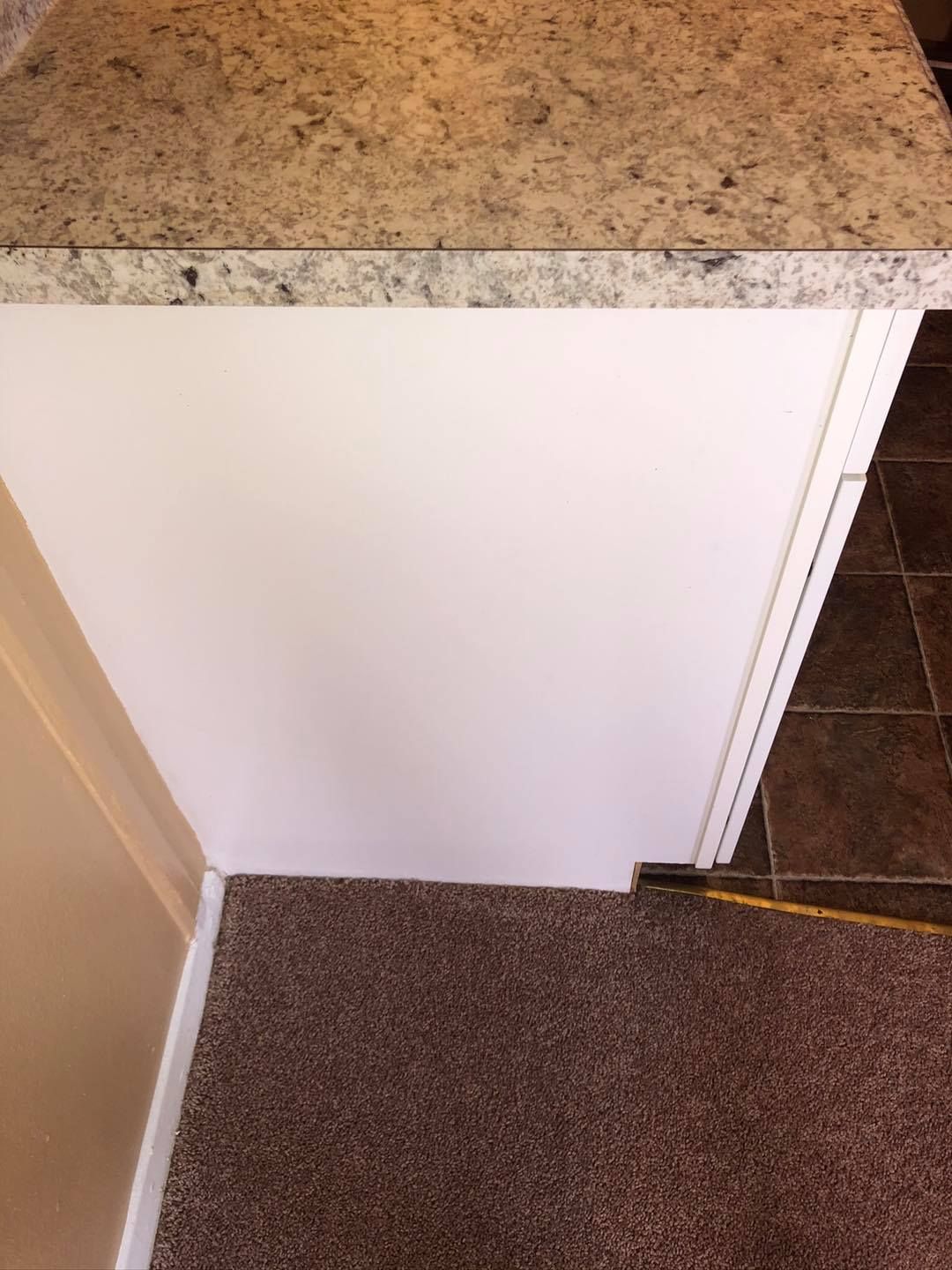 A side view of a white kitchen cabinet island with a speckled beige countertop, sitting on a brown carpeted floor.