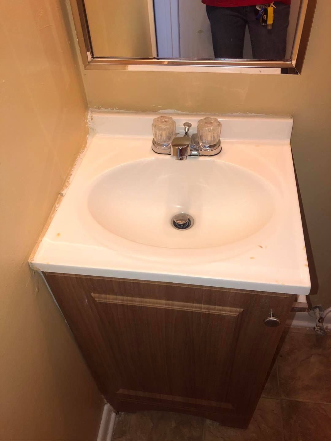 A brown wooden vanity cabinet with a white countertop, sink, and silver faucet beneath a bathroom mirror.