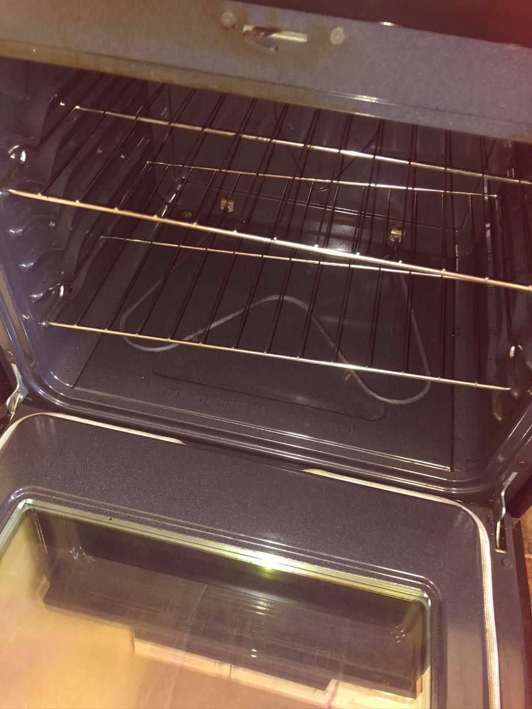 An open oven interior with a single metal rack inside, showing dark walls and a glass-paneled door.
