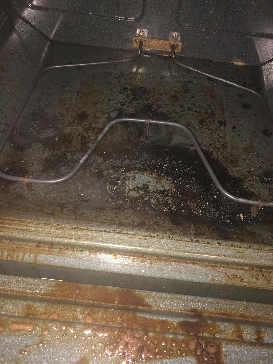 Interior of a dirty oven with a heating element, showing significant dark food residue and burnt spills on the floor.