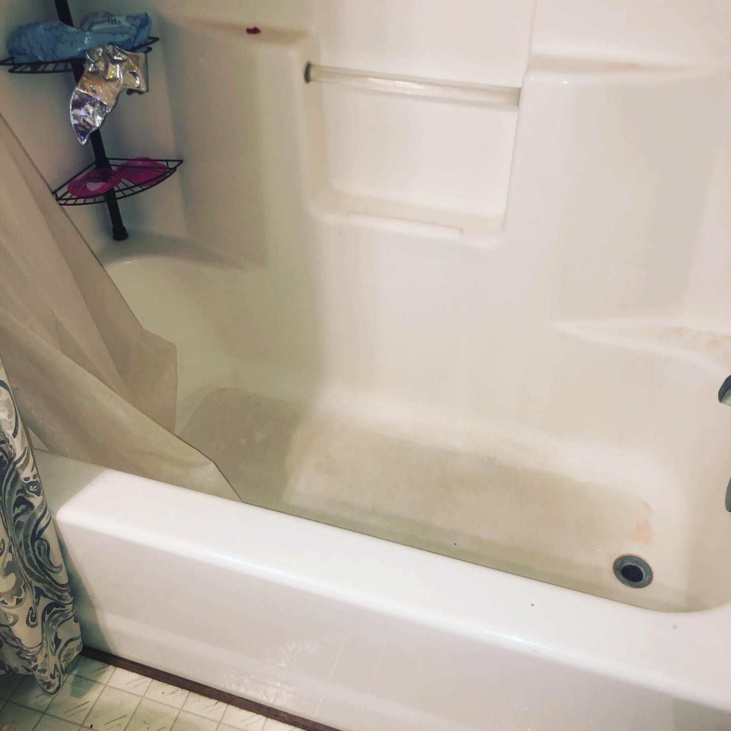 A white bathtub and shower surround with a corner storage shelf and a patterned shower curtain.
