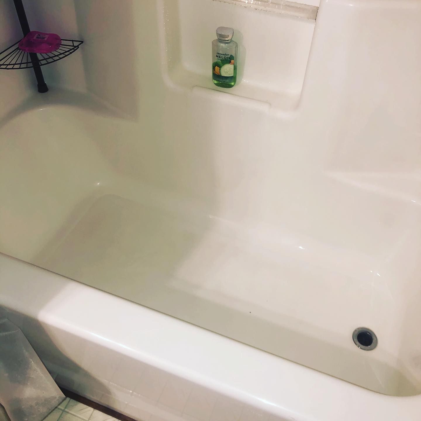 A clean white bathtub with a metal wire corner rack and a bottle of soap sitting in a built-in recessed shelf.