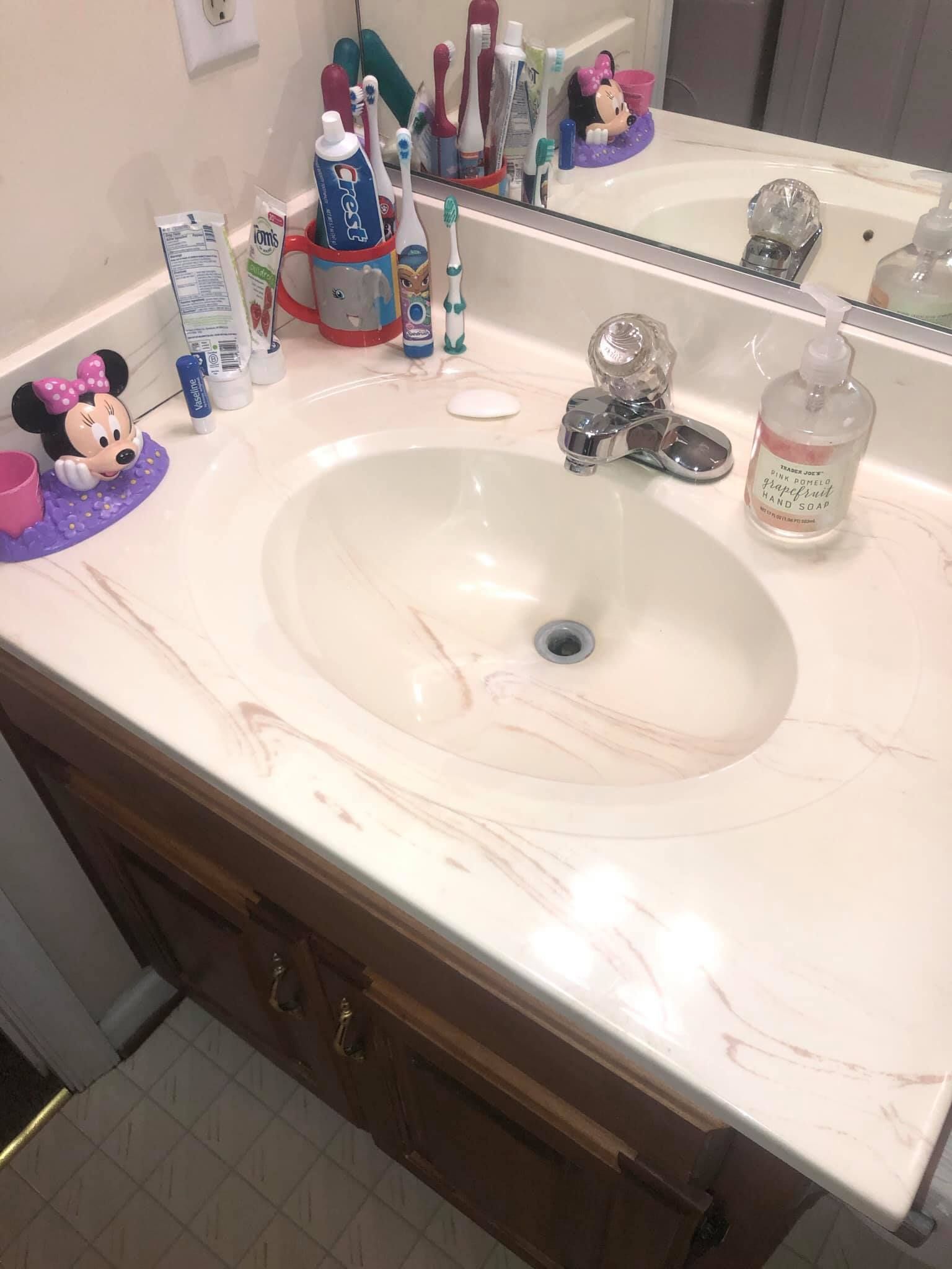 A bathroom vanity sink with a light marble countertop, featuring several toothbrushes, soap, and Minnie Mouse accessories.